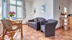 En stue med sofa, en fletstol, et bord med en blomstervase og en lampe.