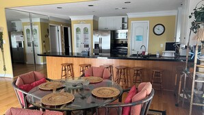 Una cocina moderna con una isla central, un área de comedor con mesas redondas de vidrio y una sala de estar con un sofá y sillones.