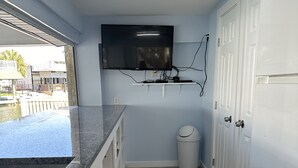 Una cocina con encimera de granito, horno empotrado, televisor de pared y un cubo de basura.