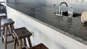 Una cocina con encimera de granito, taburetes de madera, un lavabo de acero inoxidable y un televisor de pantalla plana montado en la pared.