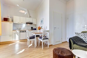 A modern kitchen with white cabinets, a dining table with chairs, and a small seating area with a couch and ottoman.