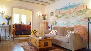 Una sala de estar acogedora con un sofá, un cofre de madera y un cuadro de un paisaje montañoso.