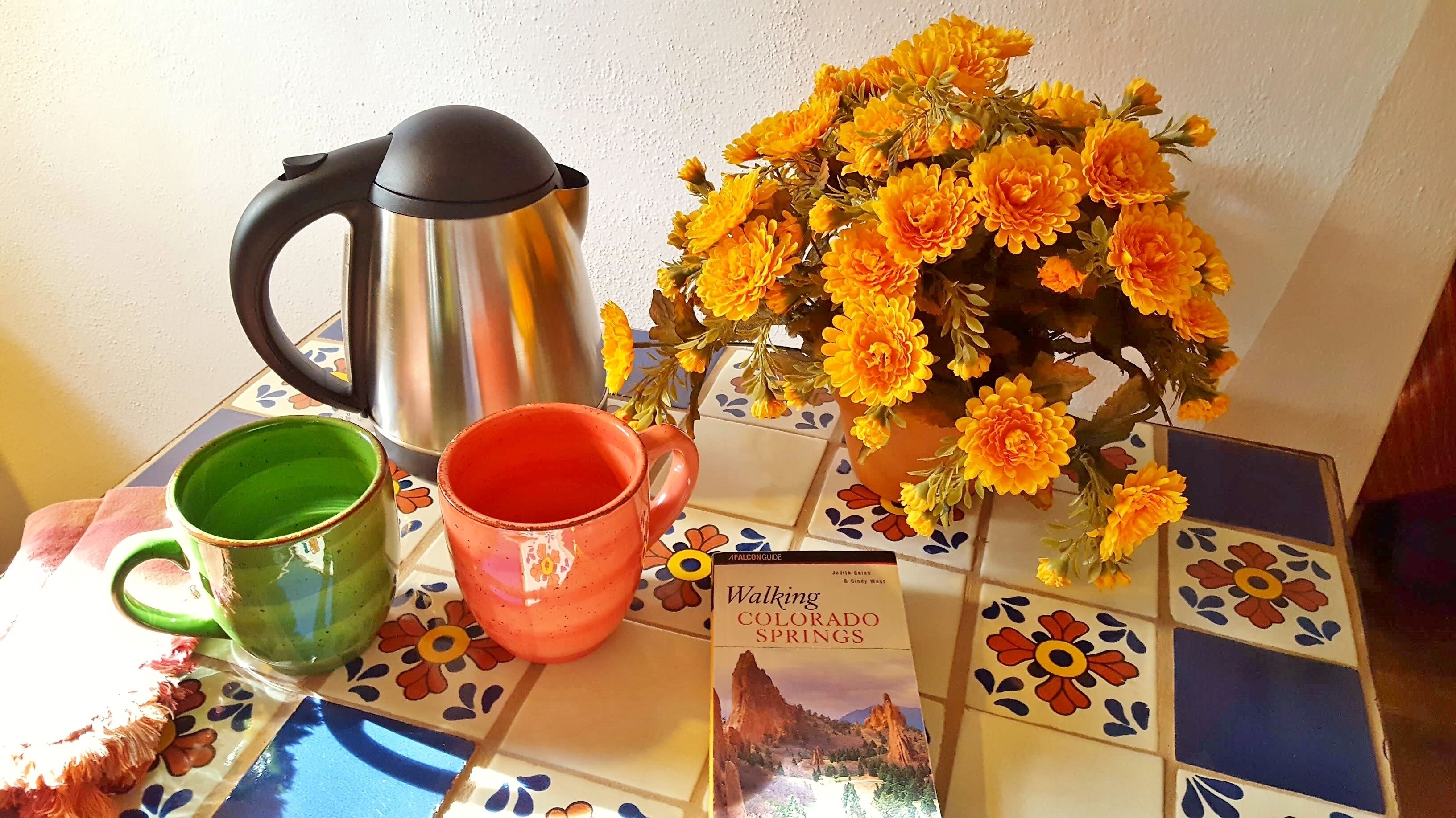 A table with a coffee pot, two mugs, a vase of flowers, and a book titled 'Walking Colorado Springs'.