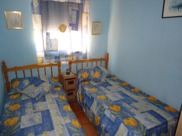 A bedroom with two beds, a nightstand, and a window with curtains.
