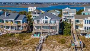 Una propiedad frente a la playa con varias casas conectadas por una pasarela de madera, con balcones y vistas directas al océano.