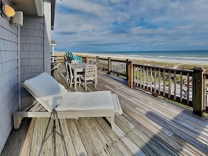 Une terrasse en bois avec un fauteuil de relaxation et une table, donnant sur une plage.