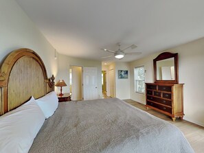 Une chambre à coucher avec un grand lit, une commode, un ventilateur de plafond et une porte donnant sur une autre pièce.