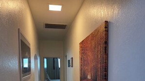 A hallway with a ceiling light, a vent, framed pictures, and a painting on the wall. - The Mountain House at the base of Mount Shasta (McCloud)