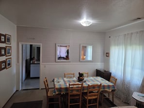 Un comedor con una mesa dispuesta para cuatro personas, sillas de madera, una lámpara en el techo y una puerta que da a otra habitación.
