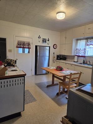 Una cocina funcional con refrigerador, una mesa de madera y una ventana con cortinas.