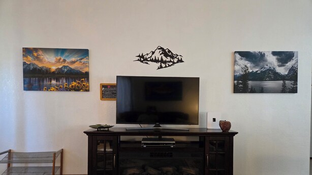A living room with a flat-screen TV, a cabinet with glass doors, and two framed landscape paintings on the wall. - The Mountain House at the base of Mount Shasta (McCloud)