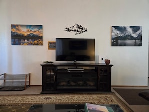 Una sala de estar con un televisor de pantalla plana, un mueble con puertas de vidrio y dos cuadros de paisajes en la pared.