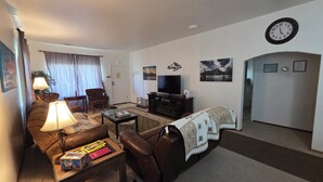 A living room with a sofa, armchair, coffee table, television, and a clock on the wall. - The Mountain House at the base of Mount Shasta (McCloud)