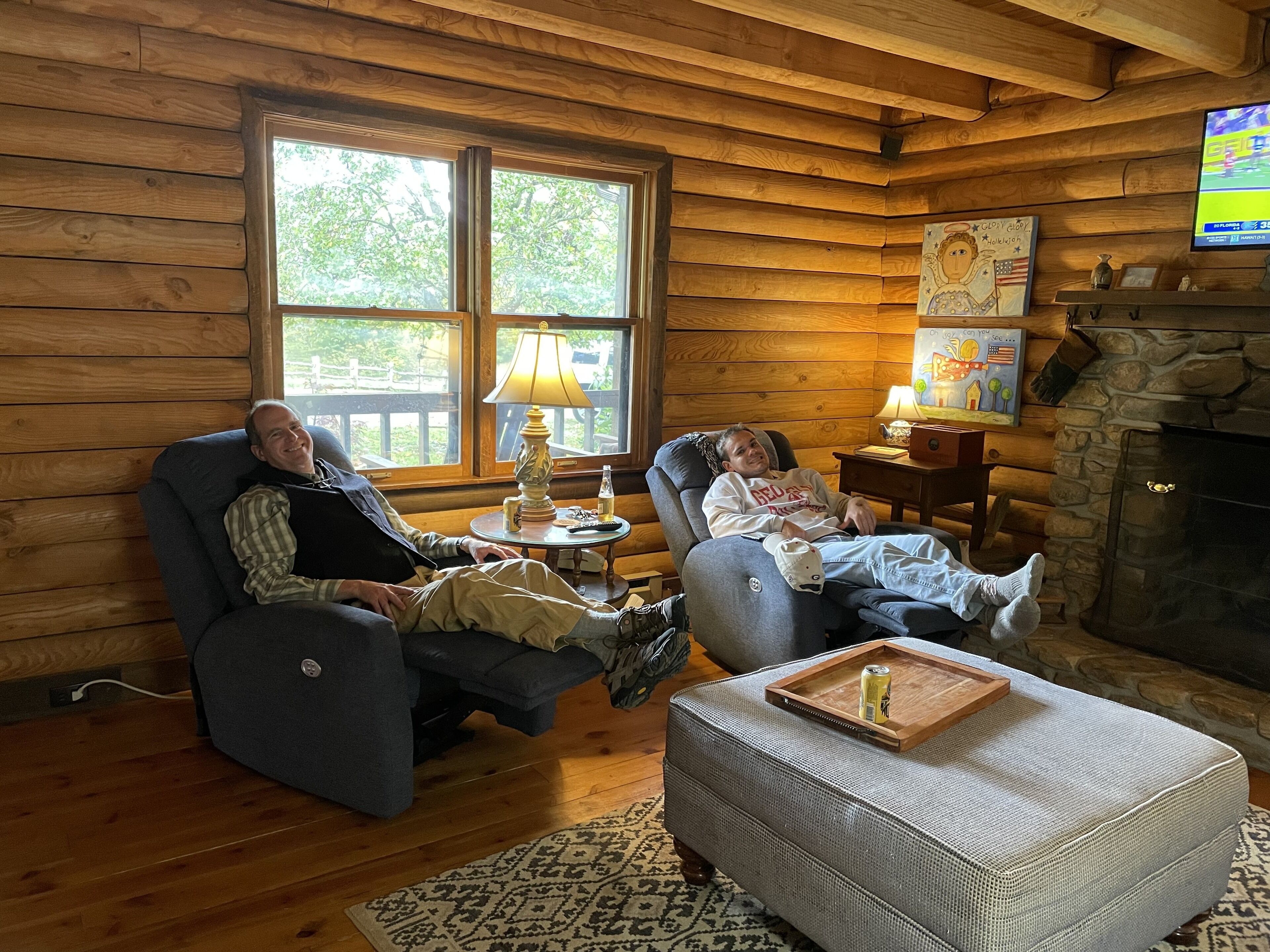 A cozy log cabin interior with a fireplace, a television, and a comfortable seating area.