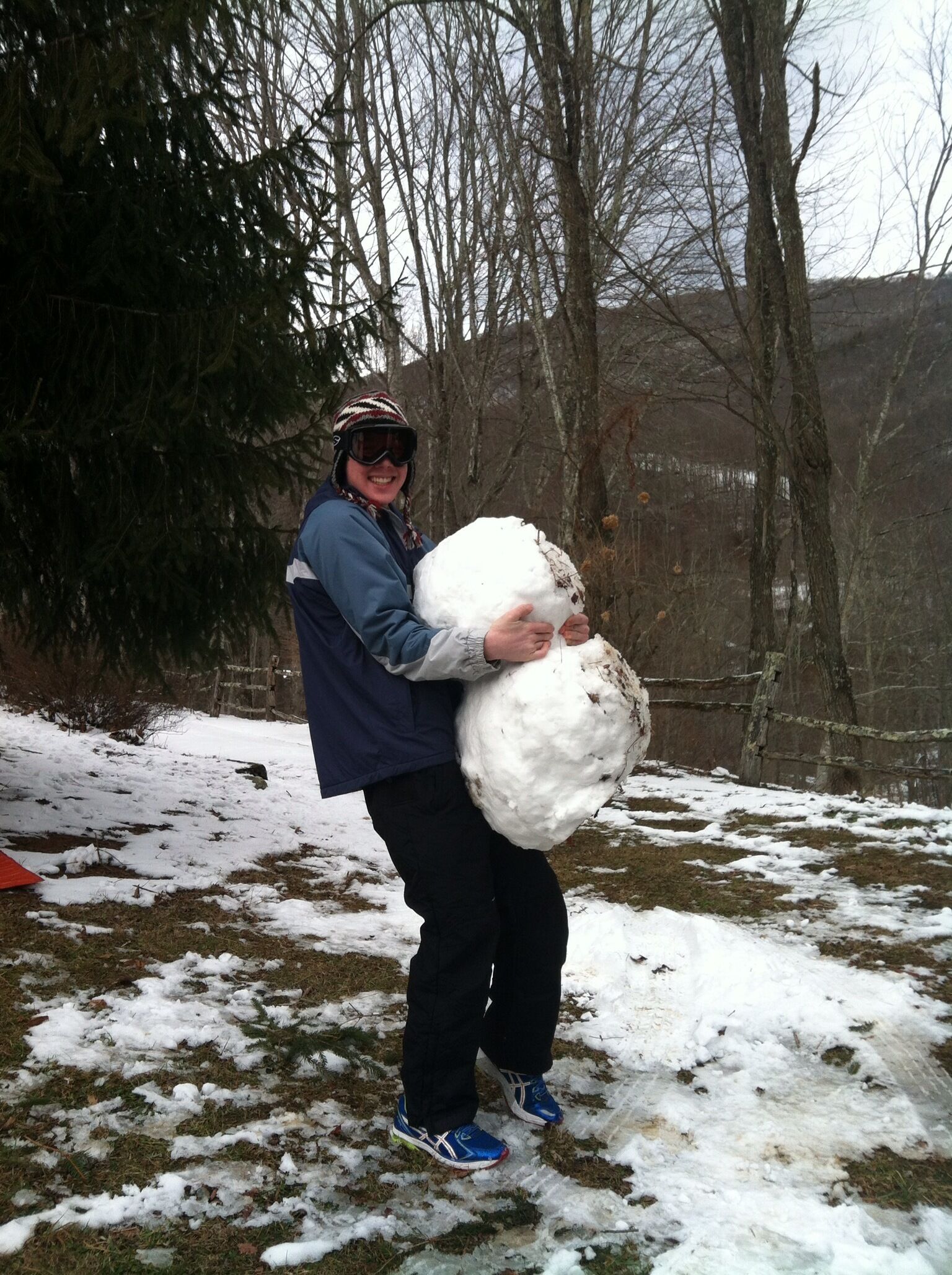 Une personne tenant une grosse boule de neige dans un décor enneigé en plein air.