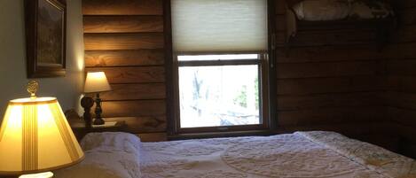 Une pièce confortable avec un lit, une lampe, une fenêtre et un tableau encadré au mur.