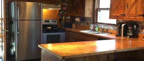 Cocina rústica con armarios de madera, un refrigerador de acero inoxidable, una barra de madera con taburetes y una ventana que proporciona luz natural.