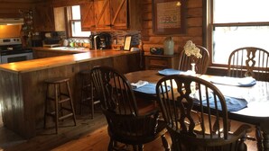 Une cuisine rustique avec des meubles en bois, un îlot central doté de tabourets, une table à manger avec des chaises et un lustre.
