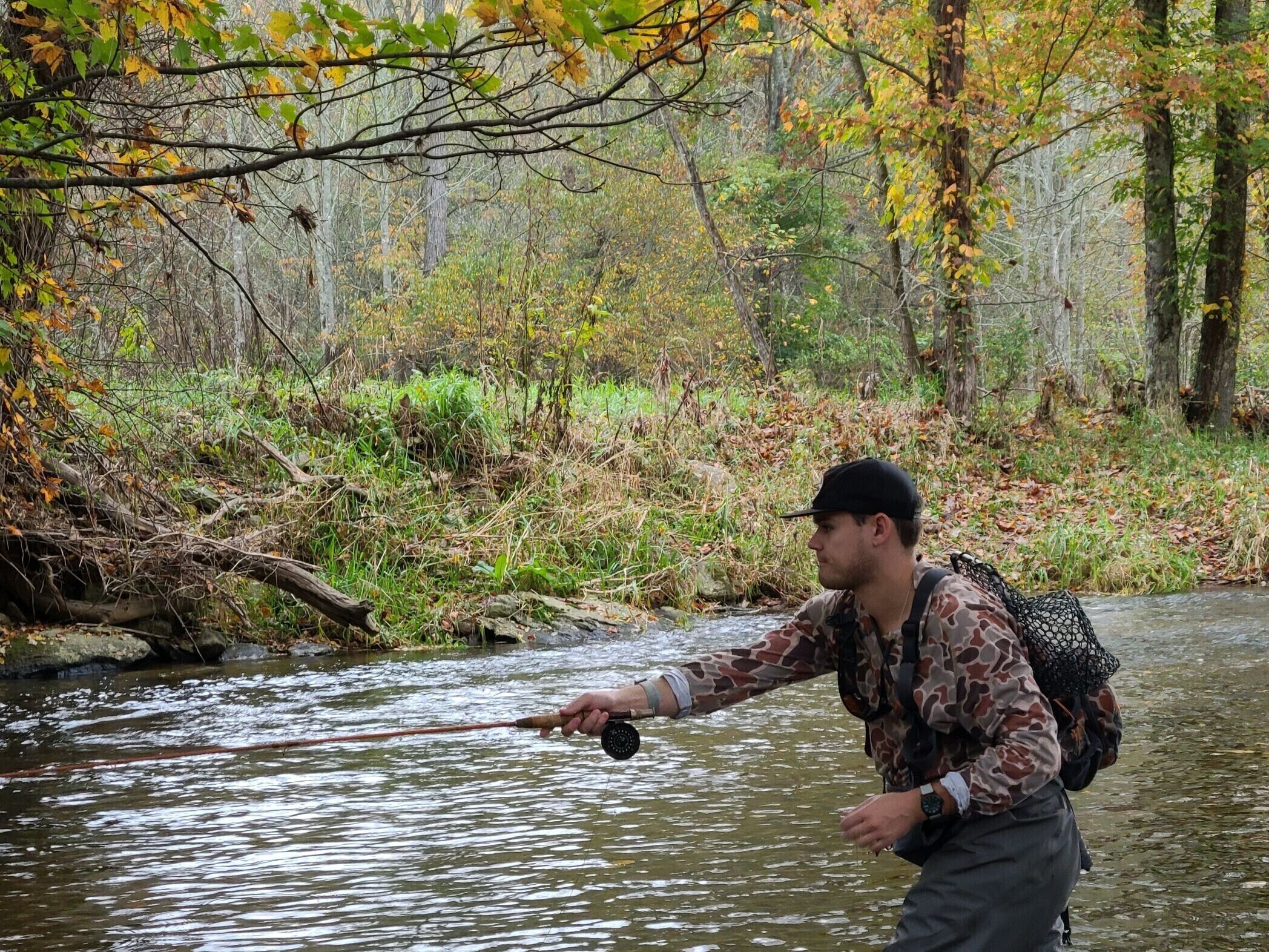 A person fishing in a river surrounded by autumn foliage.
