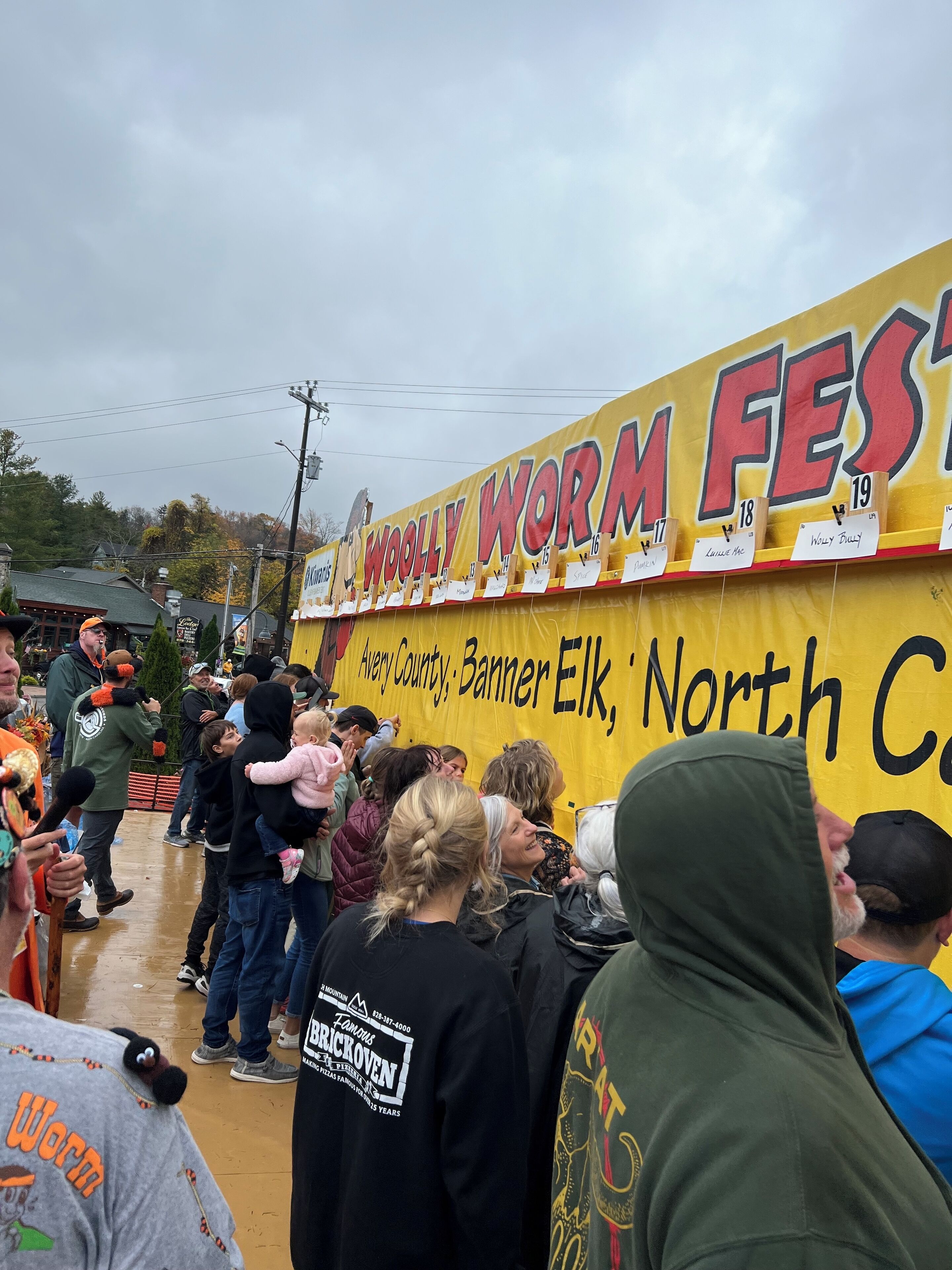 A crowd at an outdoor event with a banner reading "Woolly Worm Fest".