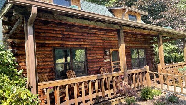 Une cabane en rondins dotée d’une véranda, de nombreuses fenêtres et d’une enseigne indiquant « Ollenville ».