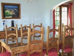 A dining area with a wooden table and chairs, a painting on the wall, and a window with curtains.