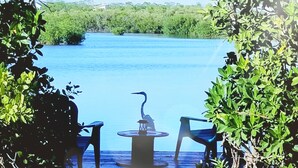 Una terraza de madera con dos sillas y una mesa, con vista a una masa de agua tranquila y vegetación densa al fondo.