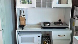 A compact kitchen with white cabinets, a microwave, a coffee maker, and a variety of kitchen utensils. - Secluded Ocean View Mid-Century Modern Retreat  (Fort Bragg)