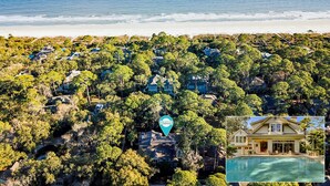 Vista aérea de una zona residencial costera con casas rodeadas de árboles frondosos y una playa al fondo.