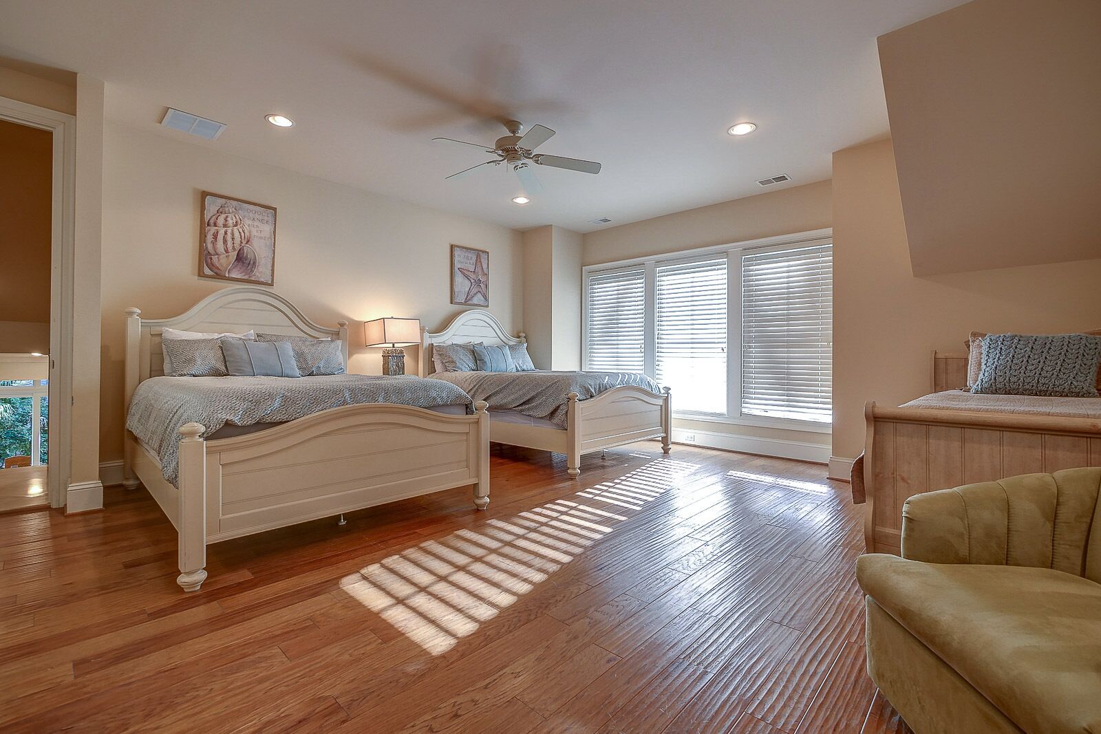 A bedroom with two beds, a ceiling fan, and a large window with blinds.
