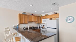 A kitchen with wooden cabinets, a granite countertop, white appliances, and a clock on the wall. - 26- Your vacation starts here in this FAMILY FRIENDLY condo that sleeps 6! (Destin)