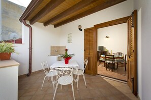 A dining area with a white table and chairs, a red vase with flowers, and a wooden door leading to another room.