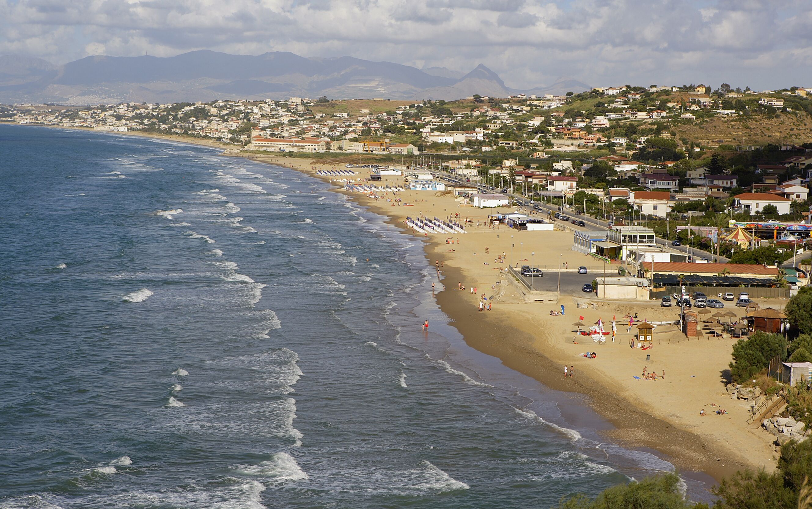 A coastal town with a beach, houses, and a mountain in the background.