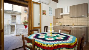 A cozy dining area with a round table covered by a colorful crochet tablecloth, wooden chairs, and a balcony with white chairs and potted plants. - THE SUN OF SICILY SEA VIEW.  WIFI FREE. WHOLE HOUSE. (Castellammare del Golfo)