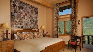 Un dormitorio con una cama grande, dos mesitas de noche, una silla, una ventana con cortinas y una obra de arte en la pared.