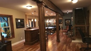 Un vaste espace de vie doté d’un plancher en bois, d’une table de billard et de tout l’équipement nécessaire pour jouer au billard.