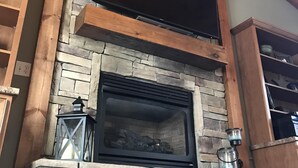 Une cheminée en pierre surmontée d’un téléviseur à écran plat, des poutres en bois au plafond et une lanterne en métal posée sur le manteau de la cheminée.
