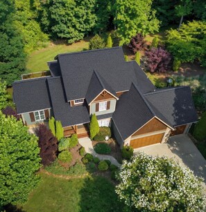A multi-story house with a sloped roof, surrounded by lush greenery and a well-maintained lawn.