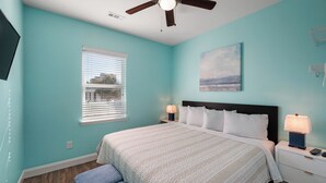 Una camera da letto con un letto, comodini, una ventola a soffitto, una finestra con persiane e un quadro appeso al muro.
