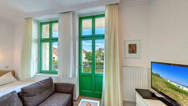 Una habitación con cama, sofá, televisor y ventana con vista a un edificio y árboles.