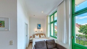 Habitación de hotel con cama, sofá, un cuadro en la pared y ventana con vistas al exterior.
