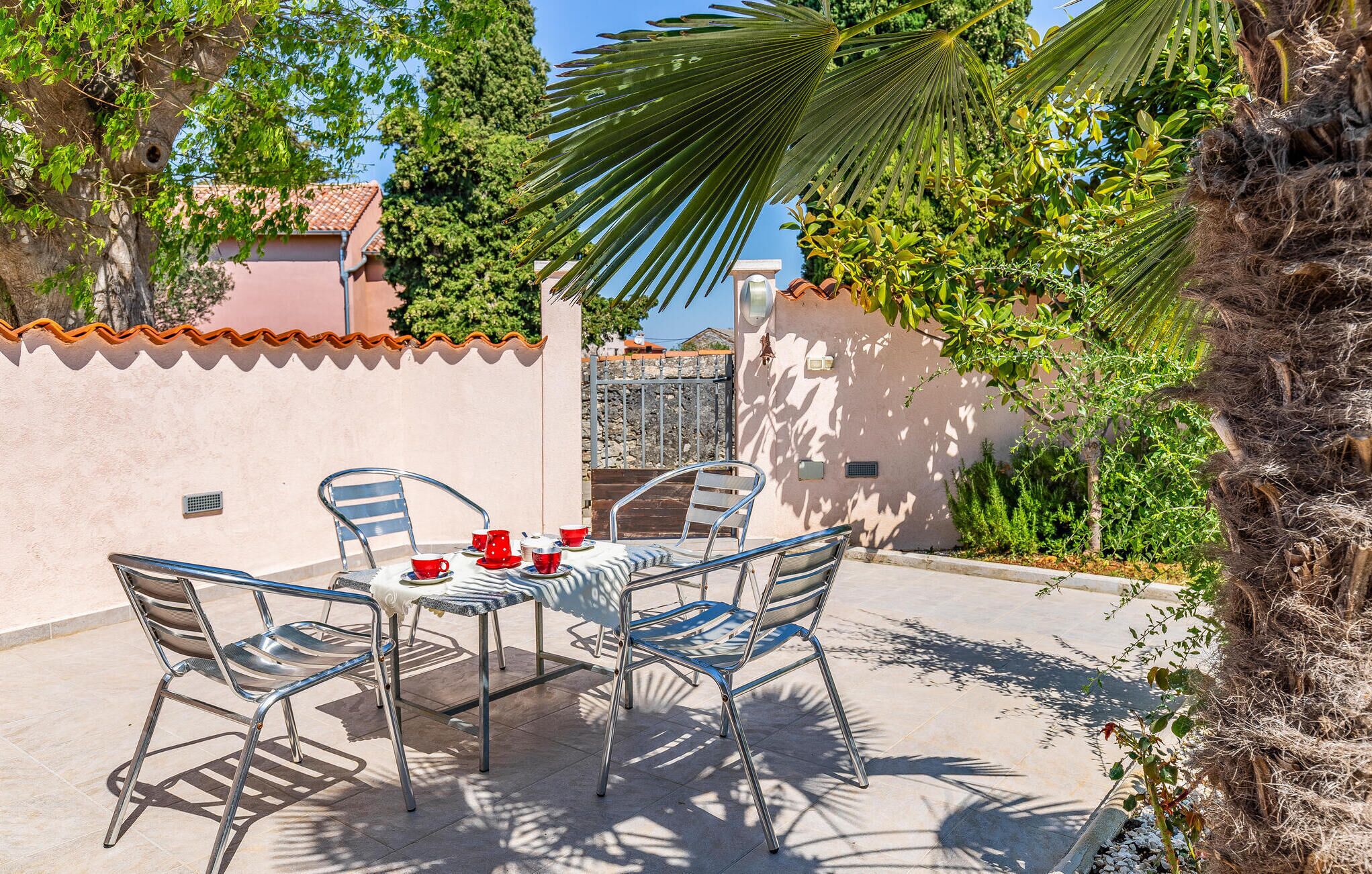 An outdoor patio with a round table and four chairs, surrounded by a low wall and various plants.