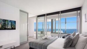 Un dormitorio moderno con una cama grande, un televisor de pantalla plana y un balcón con vistas al mar.