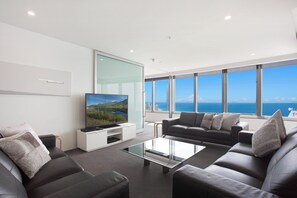 A modern living room with a large flat-screen TV, two sofas, and a coffee table.