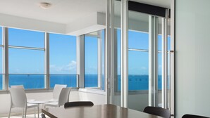 Una habitación moderna con una mesa grande y sillas, ventanas amplias con vistas al mar, y una puerta corrediza de cristal.