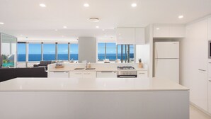 Una cocina moderna con una isla grande, armarios blancos y vistas al océano.