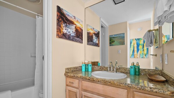 Un baño con encimera de granito, lavamanos, espejo y una obra de arte en la pared.