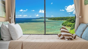 A room with a large window offering a view of a tropical beach and ocean.