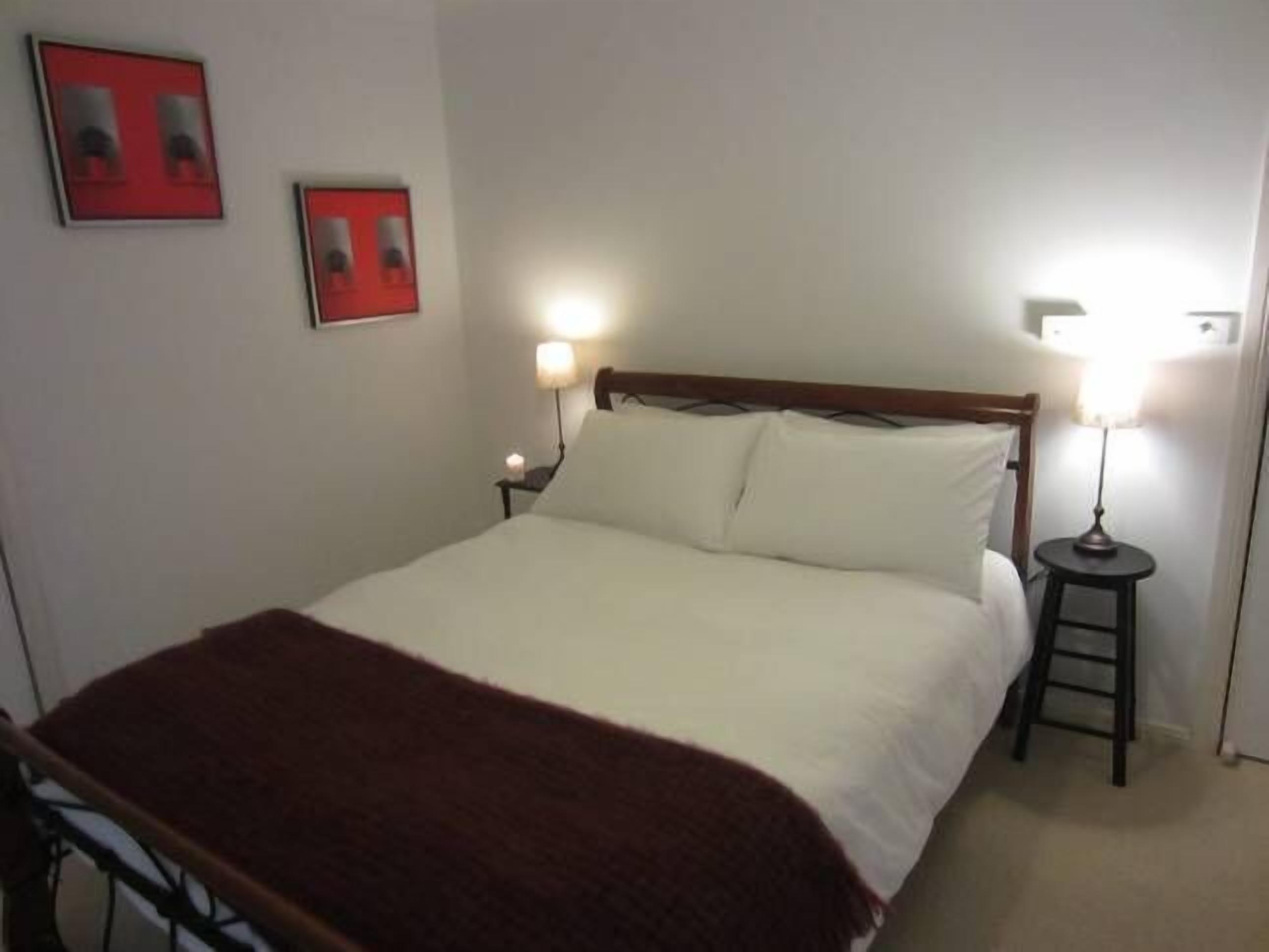 A neatly made bed with a white comforter and a brown throw blanket. There are two bedside tables with lamps, and two framed pictures on the wall.