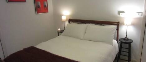 A neatly made bed with a white comforter and a brown throw blanket. There are two bedside tables with lamps, and two framed pictures on the wall.